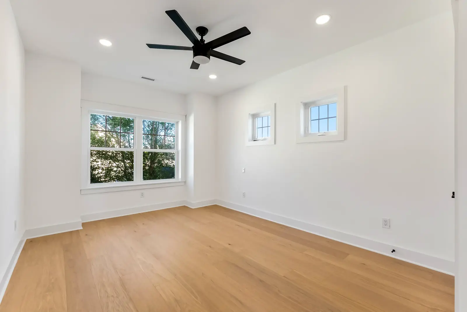 The same living room before staging: empty white walls, wood floor, large window and ceiling fan