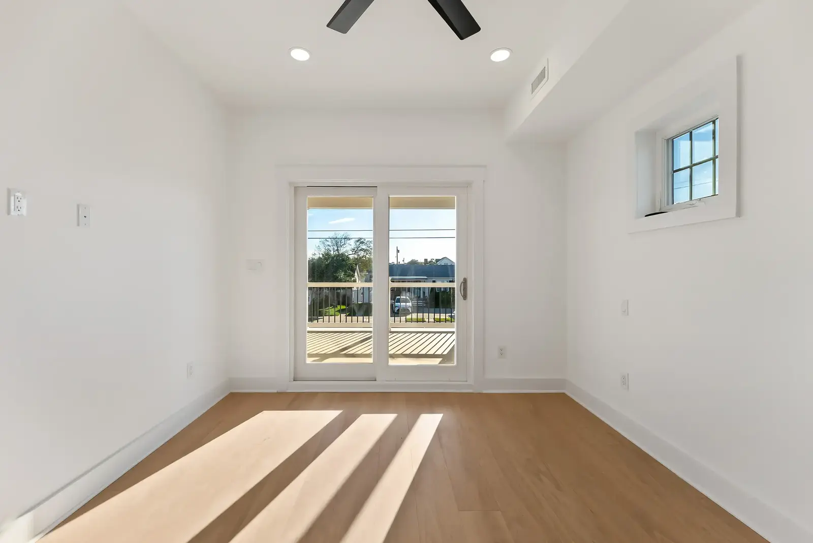 Empty bedroom with wood floors, a sliding door to a balcony and a small window