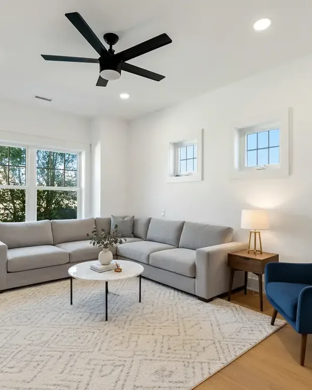 The same living room staged by the model with a sofa, rug, armchair and plant, keeping the real windows and floor